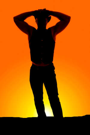 a silhouette of a cowboy with his hands on his hat in the outdoors.の写真素材
