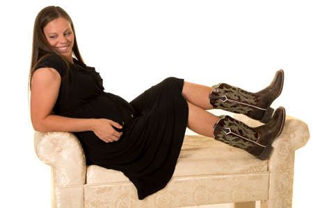 A pregnant woman stitting on a bench with her boots up on the couch.の写真素材