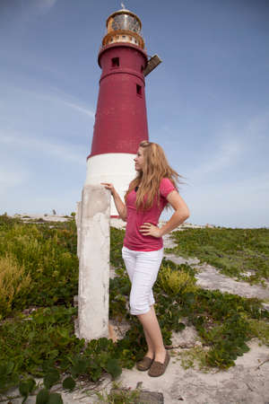 A girl standing by a red and white lighthouse with a beautiful blue sky.の写真素材