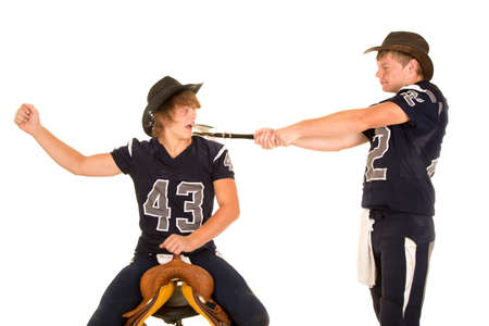 A teen cowboy in his football jersey swinging his ax at another player sitting on a saddle.の写真素材