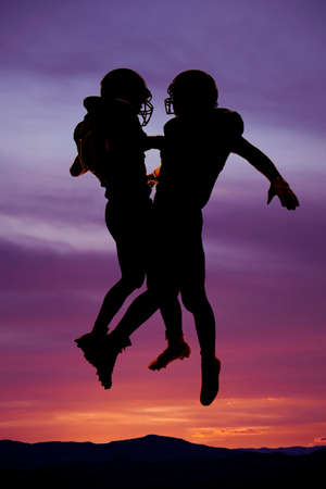 A silhouette of two football players excited about a good play, jumping and chest bumping each other.の写真素材