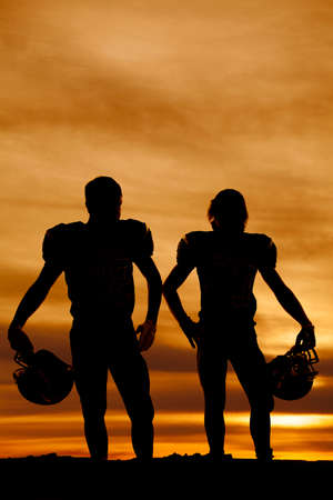 A silhouette of two football players, standing and holding on to their helmets.の写真素材