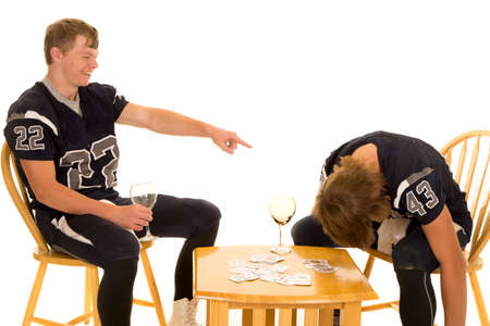 Two teen football players in their jerseys, one is pointing and lauging at the other.  They are playing a game of cards.の写真素材