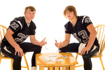 Two teen football players with cups in their hands with serious expressions on their faces, playing cards.の写真素材
