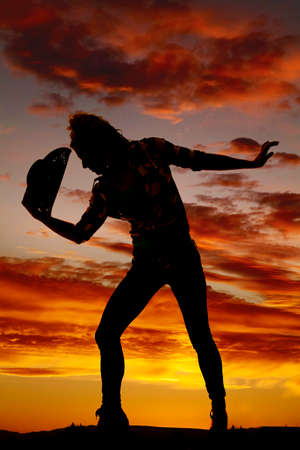 A silhouette of a woman with her hat by her head standing.の写真素材