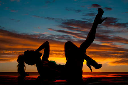 A silhouette of a woman laying on the ground with her legs up.の写真素材