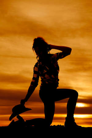 A silhouette of a cowgirl kneeling down with her western hat by her foot.の写真素材