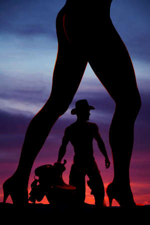 A silhouette of a womans legs with her cowboy with his saddle inbetween them.の写真素材