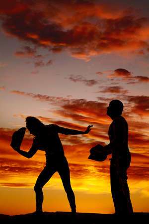a silhouette of a cowboy standing next to his cowgirl that is pushing him away.の写真素材