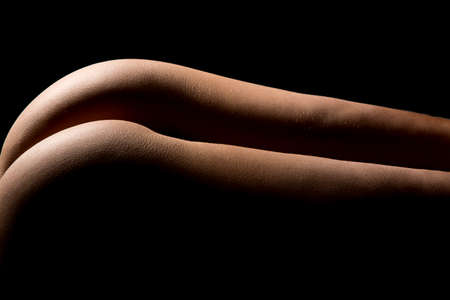 The back of a womans leggs and buttocks highlighted on a black backgroundの写真素材