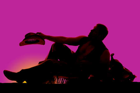 A silhouette of a cowboy leaning back on a saddle resting.の写真素材
