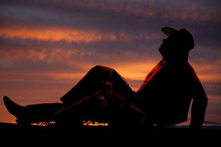 A silhouette of a cowboy sitting down and looking up.の写真素材