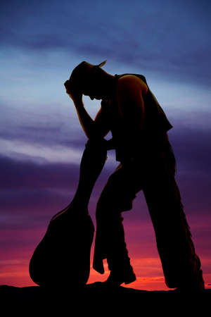 A silhouette of a cowboy leaning up against a guitar case.の写真素材