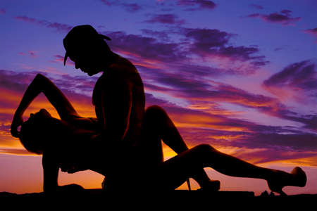 a silhouette of a cowboy holding on to his woman who is laying back.の写真素材