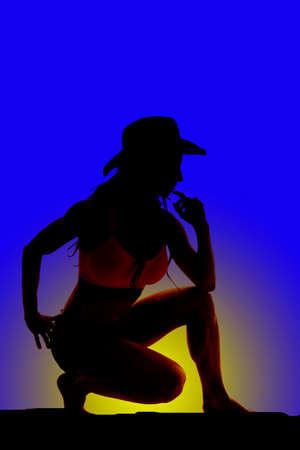 Silhouette of a sexy cowgirl on one knee in the sunset or sunrise.の写真素材