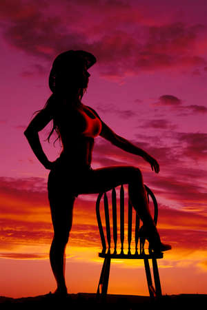 A silhouette of a cowgirl with her foot on a chair in the sunset.の写真素材
