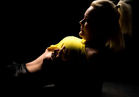a blond woman laying in the shadows pulling up her yellow top.の写真素材