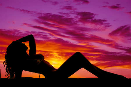 A silhouette of a woman in a bikini laying in the sunset.の写真素材