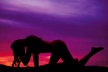A woman crawing on her knees in a bikini in a purple sunset.の写真素材