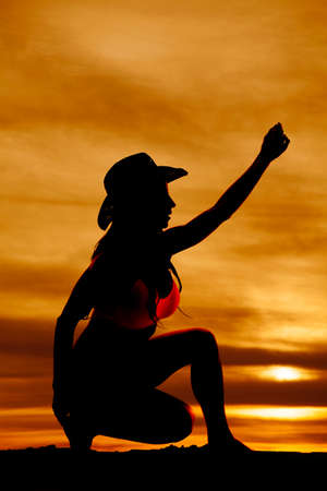 A silhouette of a cowgirl on one knee reaching up.の写真素材