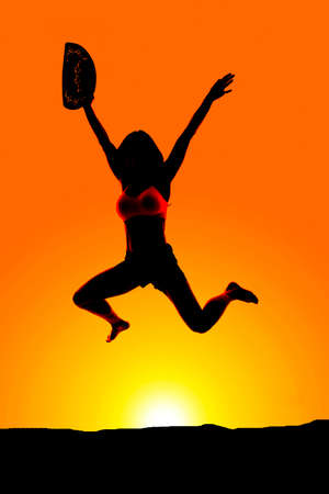 A silhouette of a cowgirl jumping with her hat in her hand.の写真素材
