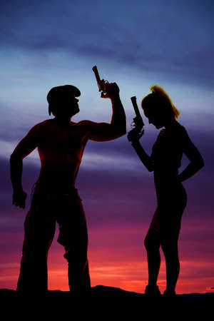 A silhouette of woman with a pistol, standing next to her cowboy who is holding on to a gun.の写真素材
