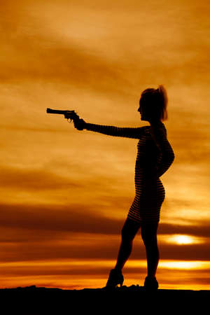 A silhouette of a woman pointing her weapon at something in the outdoors.の写真素材