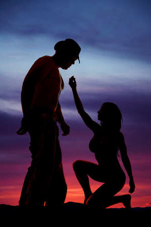A silhouette of a woman kneeling and reaching up to her cowboy.の写真素材