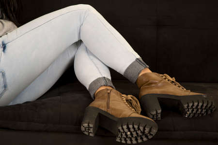 a woman sitting on her couch with her legs curled up and her boots on the couchの写真素材