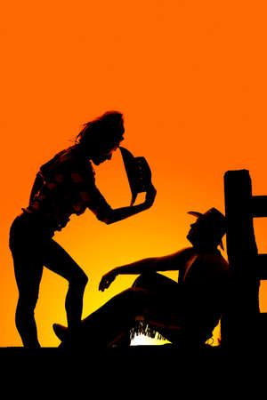 a silhouette of a woman bending down with her western hat off, looking at her cowboy who is sitting by the fence.の写真素材