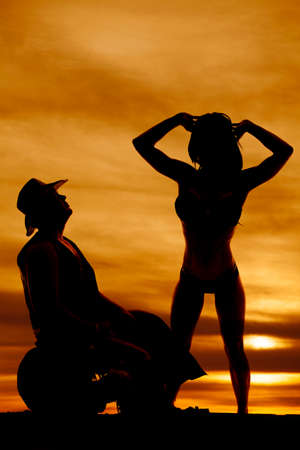 a silhouette of a cowboy kneeling down, next to his woman who has her arms up.の写真素材
