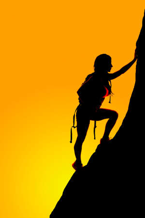 A silhouette of a woman in her backpack climbing the side of a mountainの写真素材