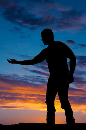 A silhouette of a man reaching out his hand toward something in the outdoors.の写真素材