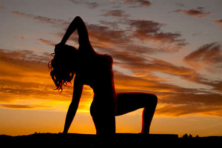 A silhouette of a woman on her knee, bending back.の写真素材