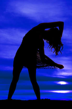 A silhouette of a woman bending over, holding out the hem of her skirt.の写真素材