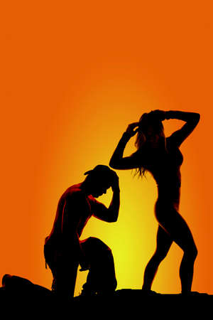 a silhouette of a woman looking back while her cowboy is kneeling to pray.の写真素材