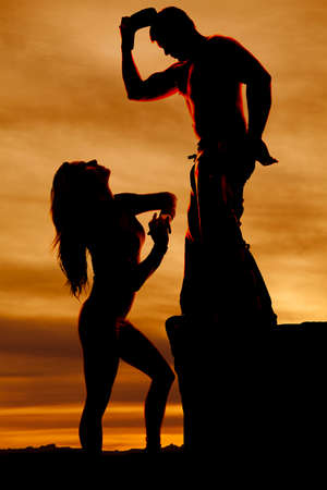 a silhouette of a woman looking up at a cowboy who is standing up on a rockの写真素材