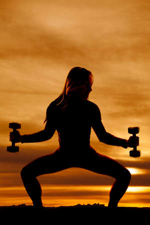 a silhouette of a woman doing a squat holding out her weights.の写真素材