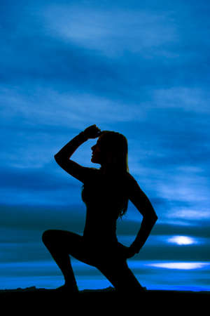 A silhouette of a woman kneeling with  her hand up by her head.の写真素材