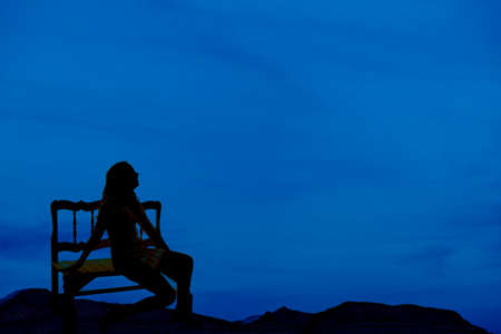 A silhouette of a woman sitting on a bench, looking up to the sky.の写真素材