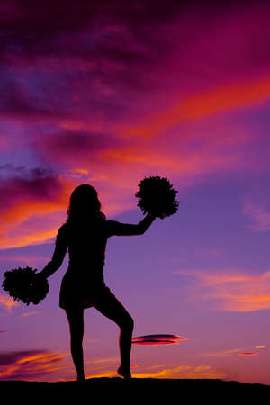 A silhouette of a woman cheerleader with her pom poms in the outdoors.の写真素材