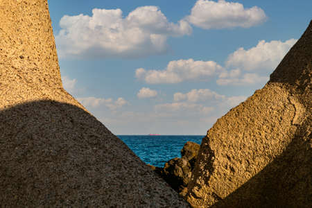Volcanic rocks, dark blue sea and cargo ship on the horizon.の写真素材