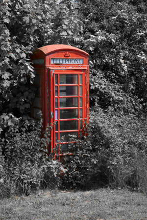 Close upright mono and color pop photograph of a single isolated overgrown out of use telephone box. red color color pop against monoの写真素材