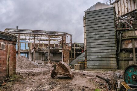 A demolition site of an old factory with rubble and steelwork with a bucket from an excavator  in the foreground and no machineryのeditorial素材