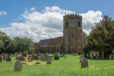 A horizontal image of a typical english country village church standing in a cemetery and taken on a sunny day with a blue skyのeditorial素材