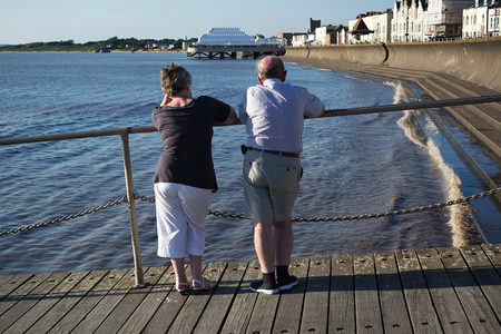 Elderly couple at the seaside standing looking at sea and pier in a british townのeditorial素材