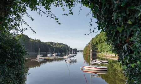 A landscape view of Rudyard lake in Staffordshire. The scene is taken with the hedge framing boats with reflections moored up on the waterの写真素材