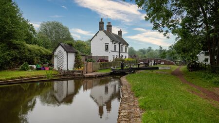 a lock keepers cottage is reflected in the still waters of the canal