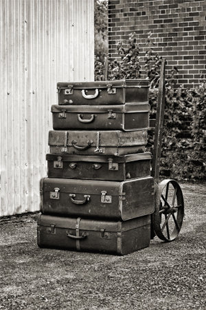a collection of old leather suitcases on a sack truck in this retro style photograph. The image is mono with a hint of sepia to give a nostalgic feelの写真素材