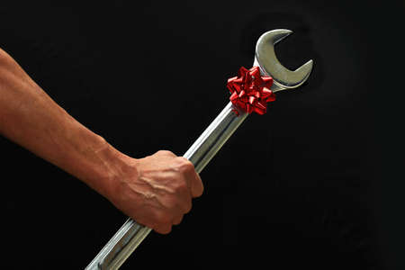 Man holding a large wrench with a red bow on it.